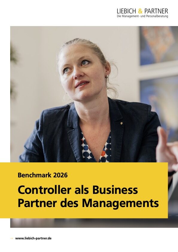 Eine Frau mit blonden Haaren in einem Blazer diskutiert und gestikuliert in einem Büro, während auf dem Hintergrund ein Plakat mit dem Titel "Benchmark 2026: Controller als Business Partner des Managements" zu sehen ist.
